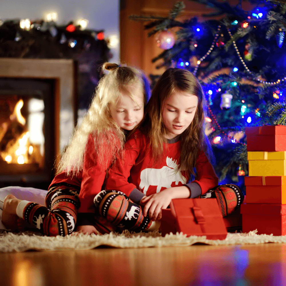 Jolly Jammies home page image. Photo shows two girls sitting under a Christmas tree wearing matching Christmas pyjamas.